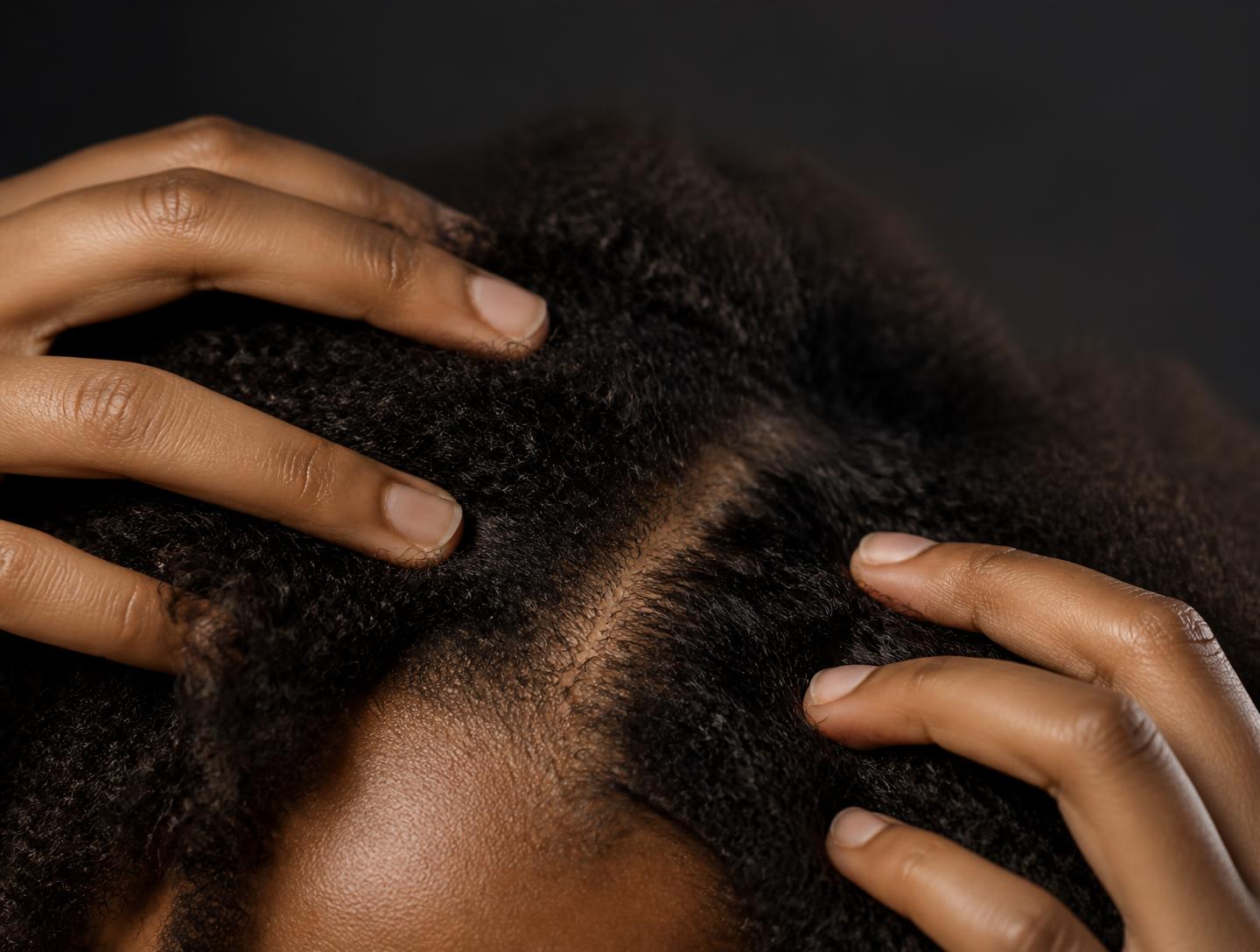 Close-up of natural coily Black hair being gently parted to show a healthy scalp